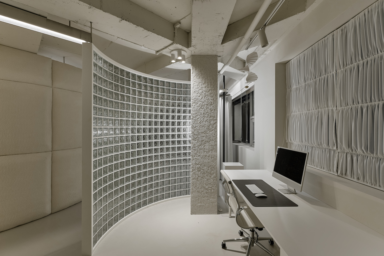 Workstation with glass block curved wall, exposed concrete ceiling beams, and white fabric panels