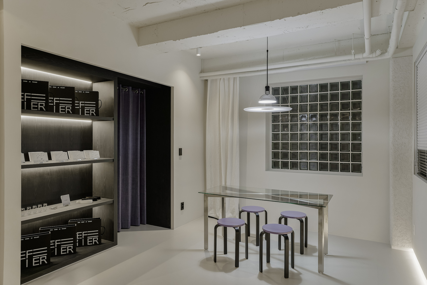 Display area with glass table, purple stools, glass block window, and black illuminated shelving