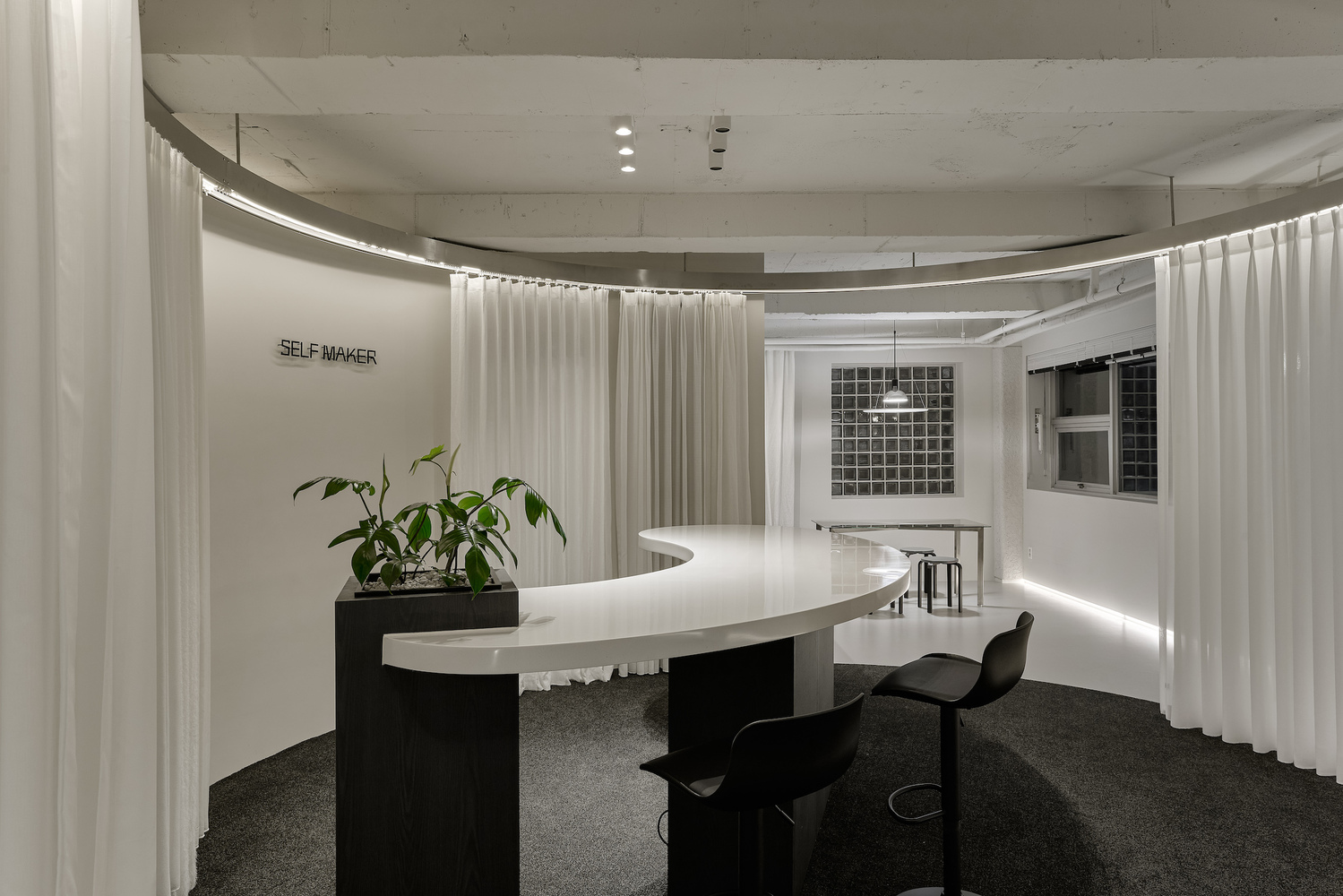 Curving service counter with potted plant, black chairs, and circular white curtain backdrop