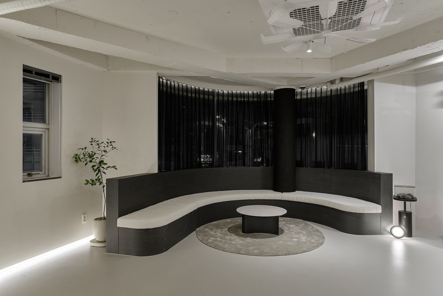Curved black reception counter with white seating ledge and central table under exposed concrete ceiling