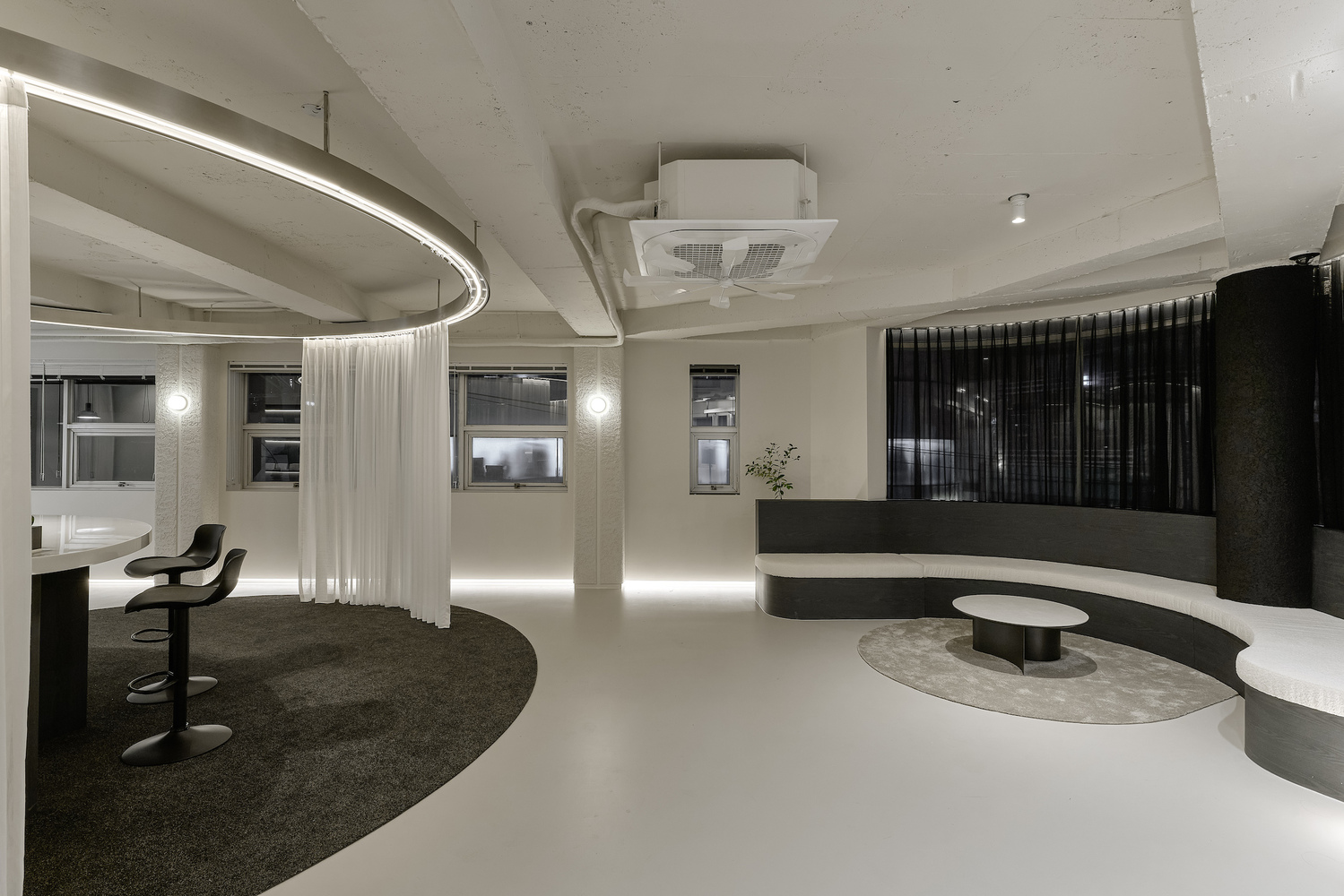 Interior with circular curtain partition and curved illuminated reception desk alongside potted plant