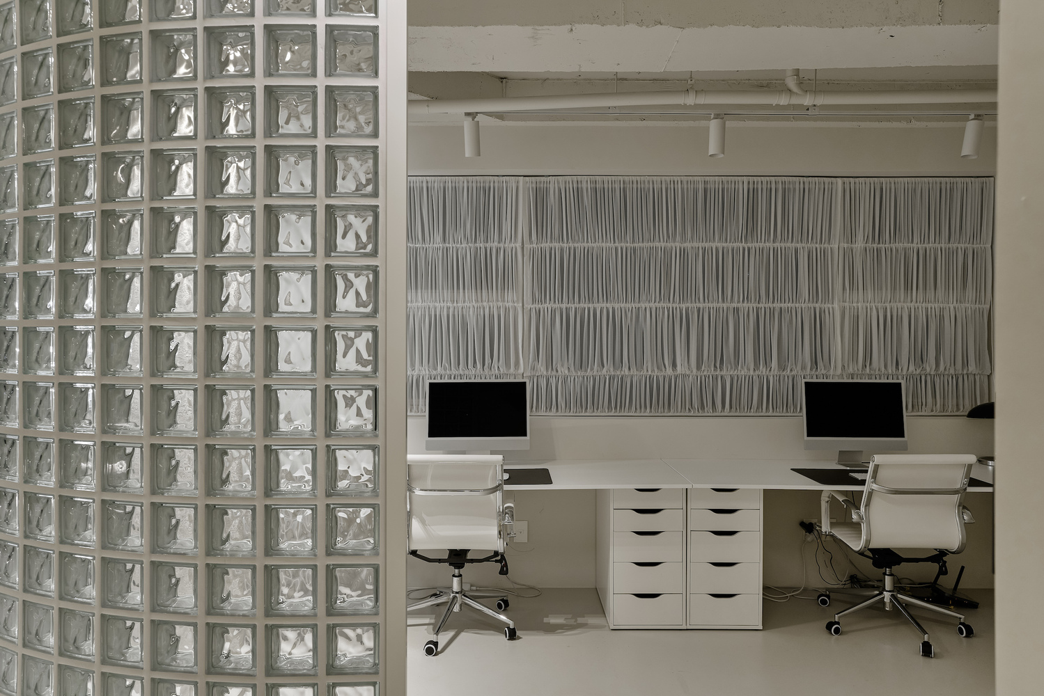 Work area with white desk units and textured wall panels behind glass block partition