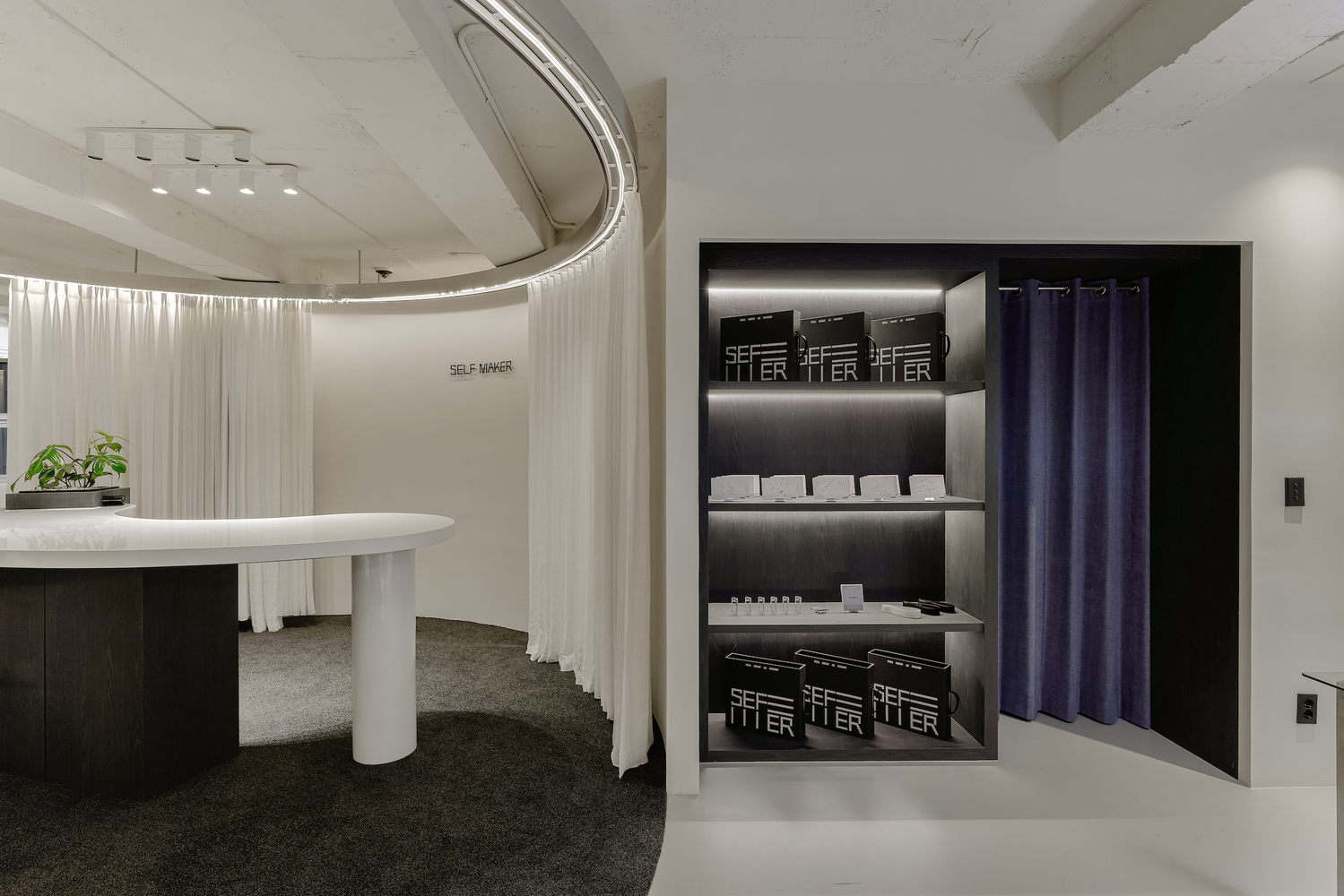 Display alcove with illuminated shelving and purple curtain beside curved reception counter