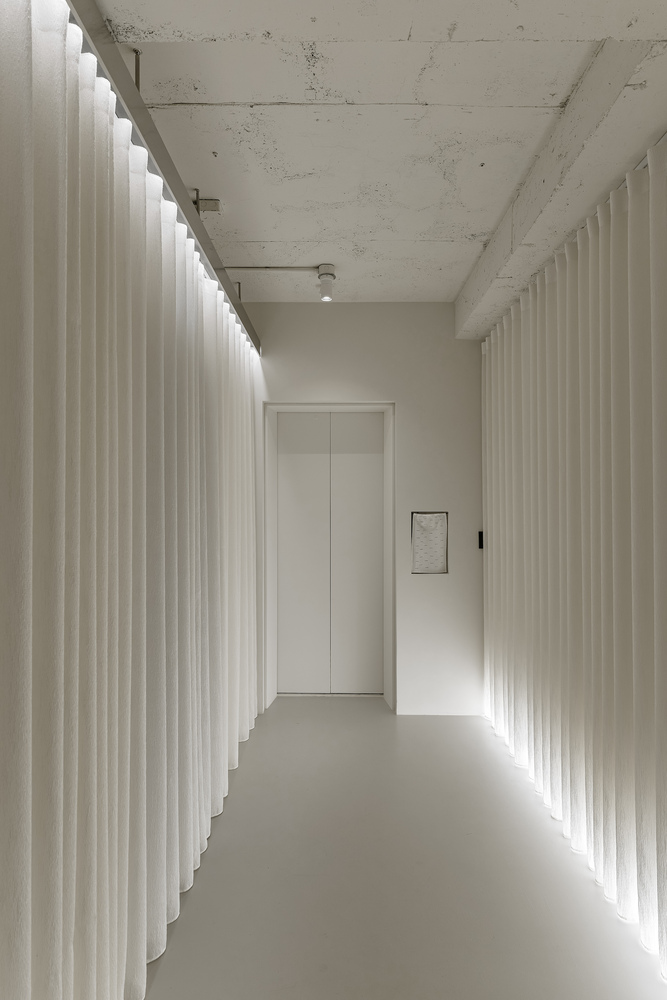 Corridor with backlit pleated curtain walls and exposed concrete ceiling beams