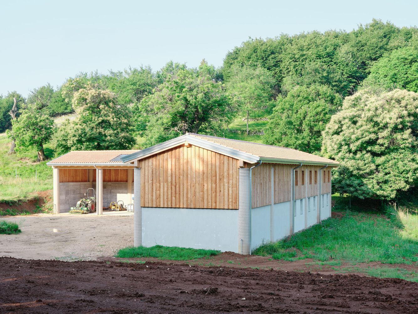 Side elevation showing the timber and concrete shed with gabled roof against wooded slopes