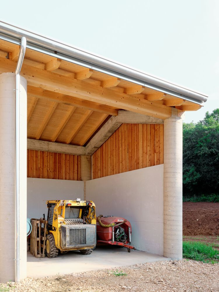 Covered corner bay with sloped timber ceiling and cylindrical columns framing machinery on gravel floor