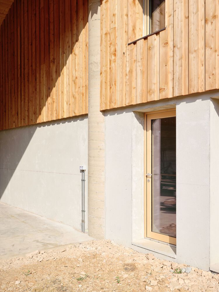 Close-up of the timber siding and white concrete wall junction with glazed door in diagonal sunlight