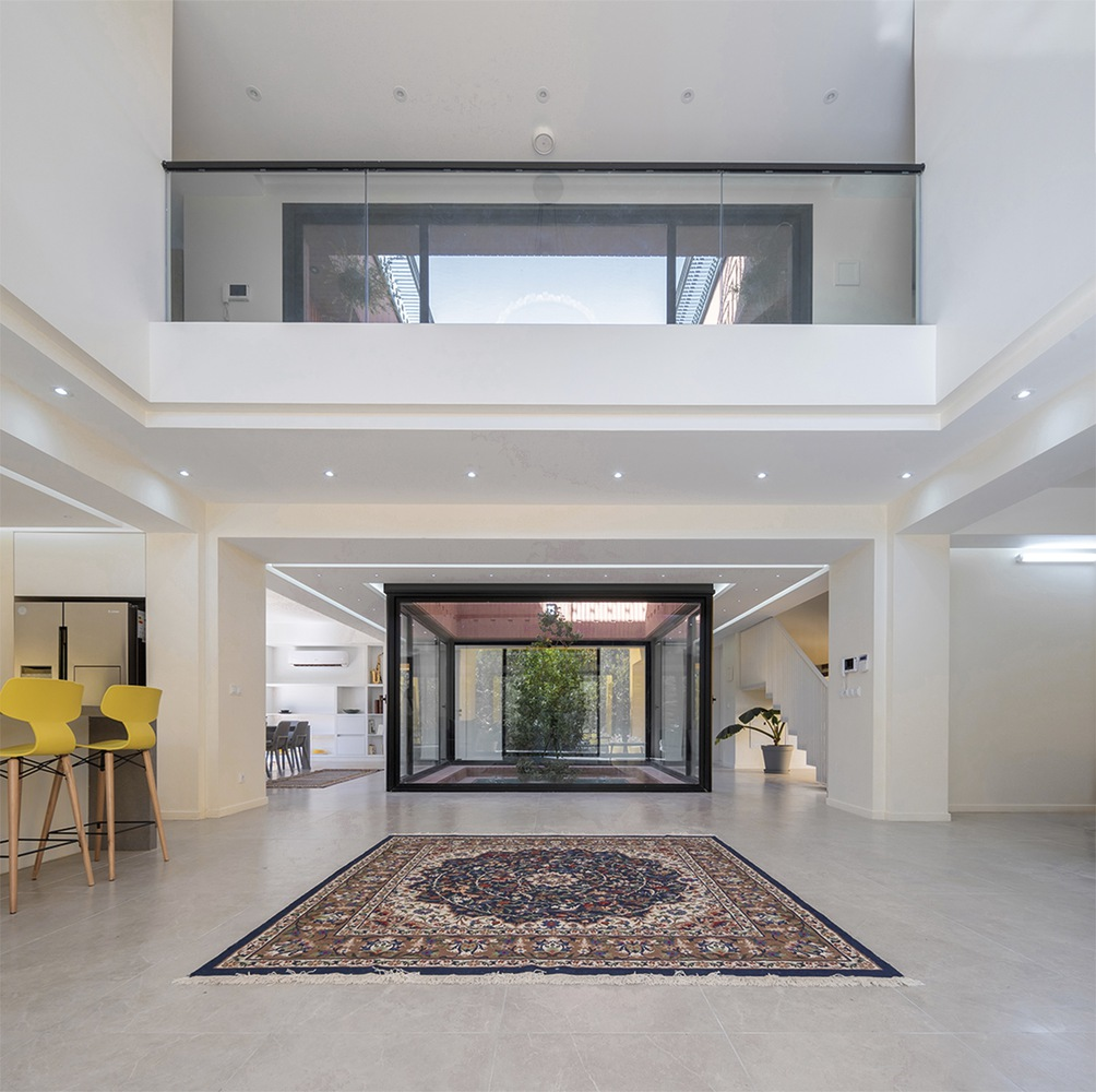 Double-height interior hall with glass-enclosed courtyard and traditional patterned rug on polished tile floor