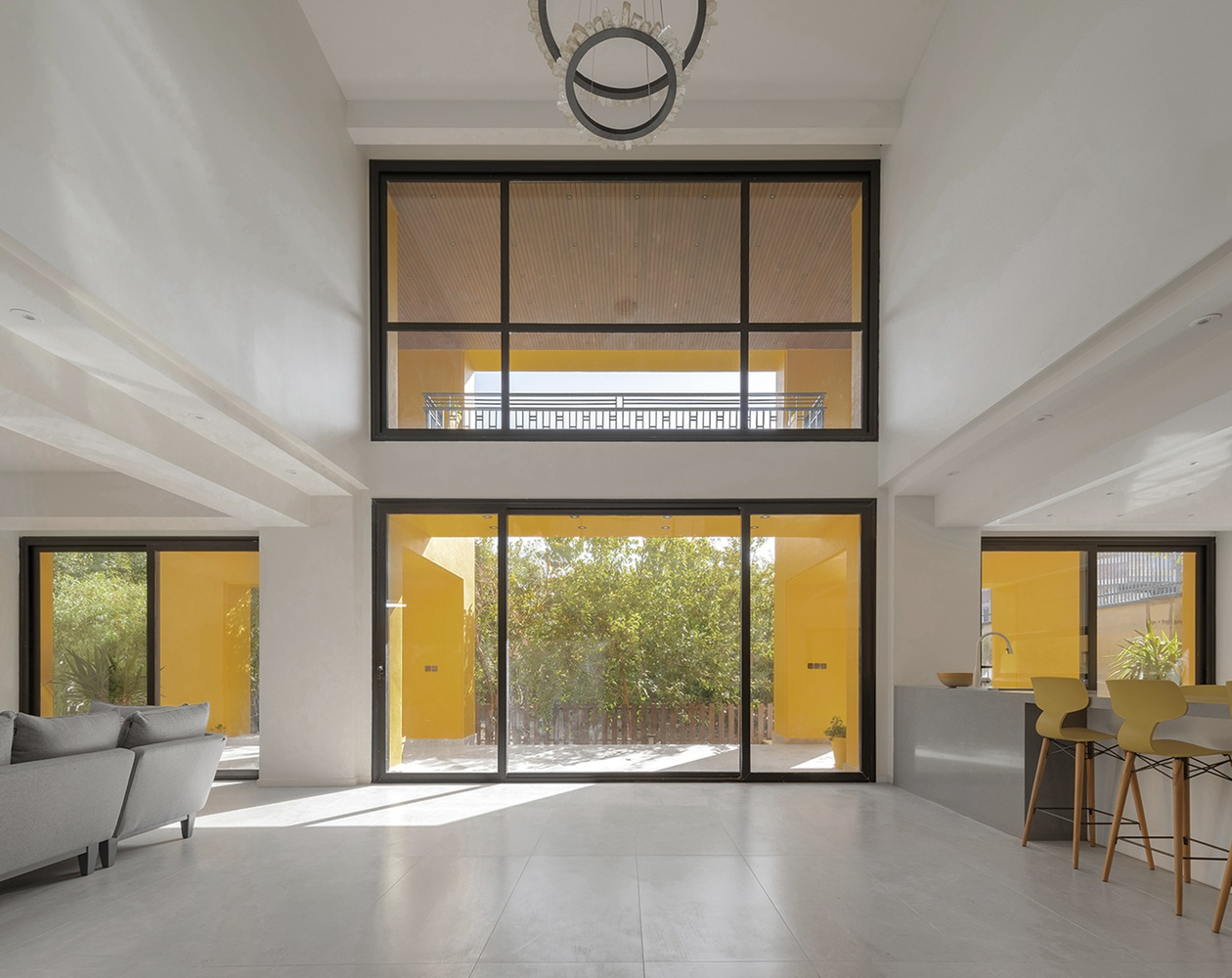 Living space with stacked horizontal windows framing yellow exterior walls and courtyard trees in daylight