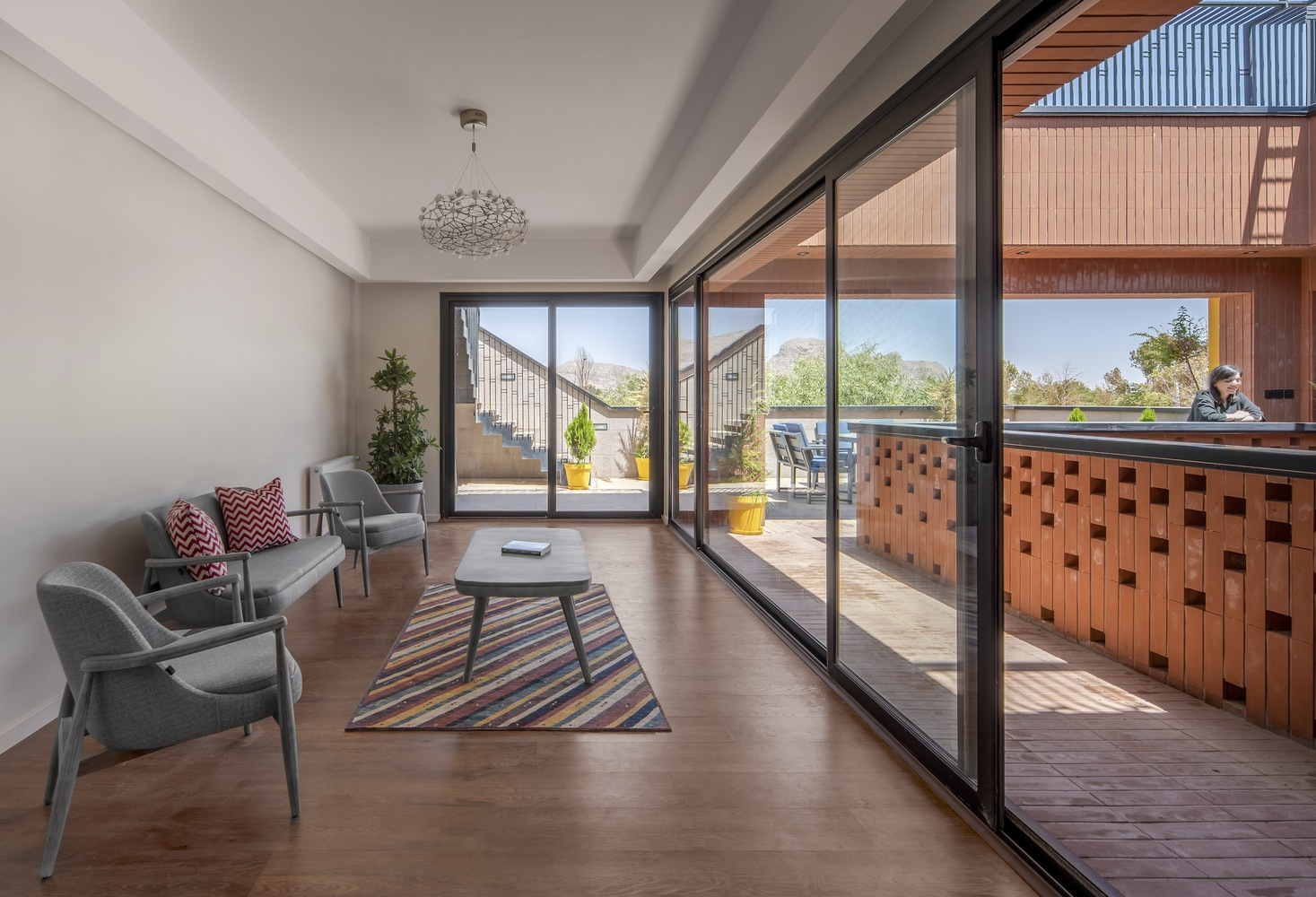 Interior living room opening through sliding glass doors to a terrace with chequered brick screening under bright daylight