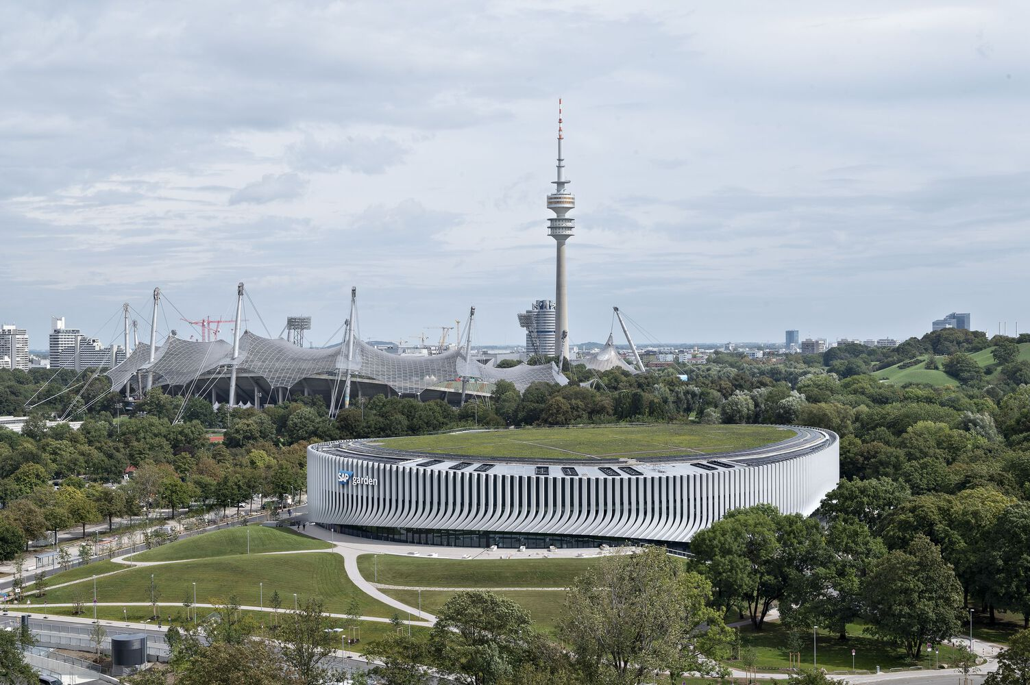 Aerial view of the oval building with vertical white and grey striped facade set in parkland