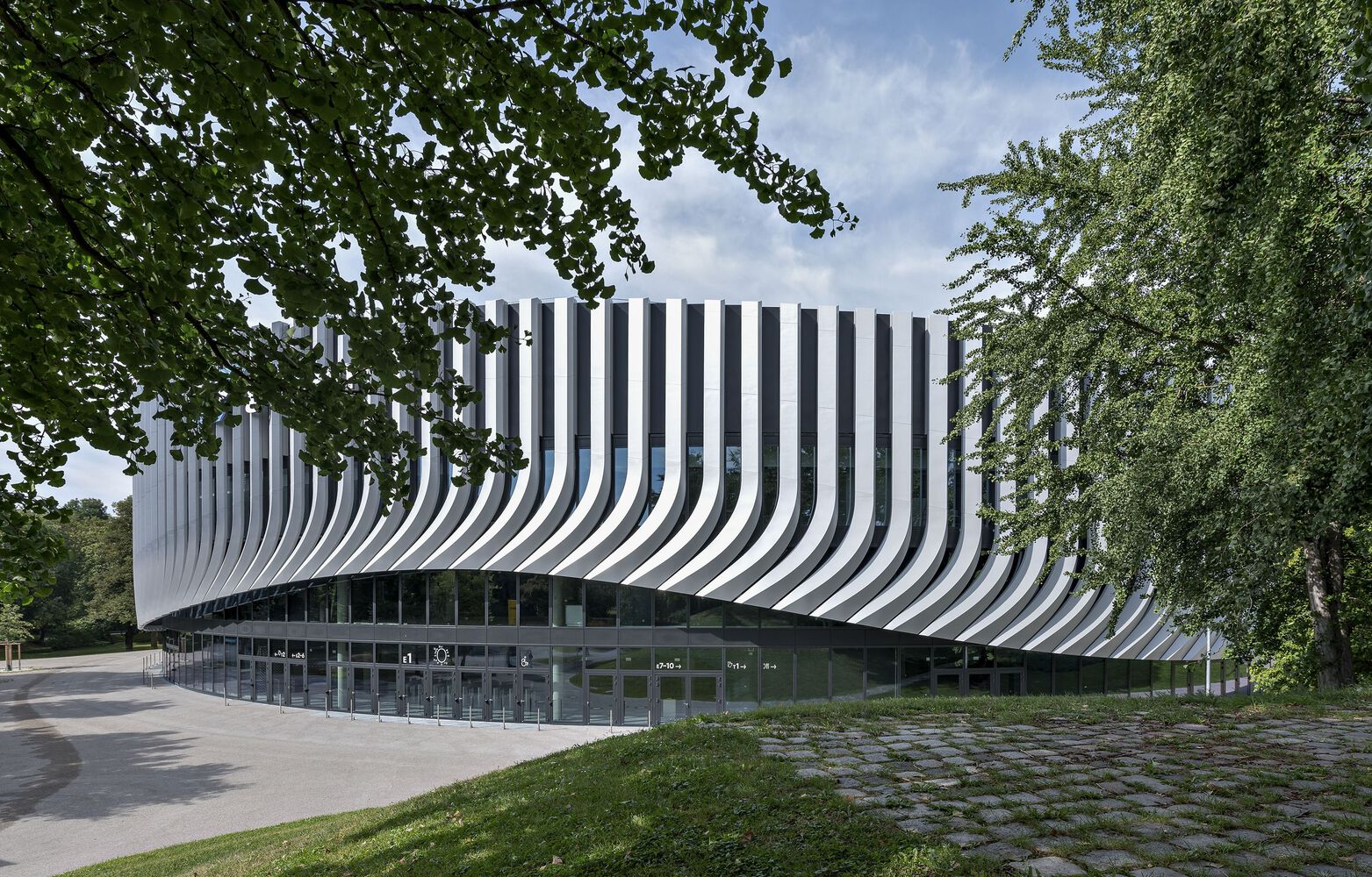 Side elevation showing the full sweep of vertical fins above the recessed glass base framed by trees