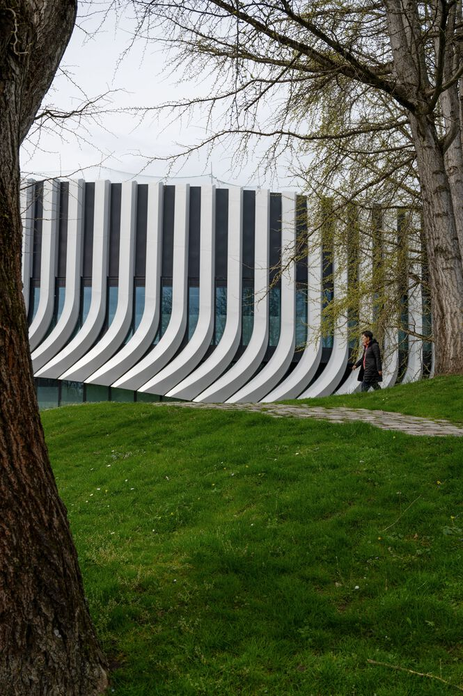 Striped white and grey facade with vertical undulating fins framed by bare tree branches in early spring