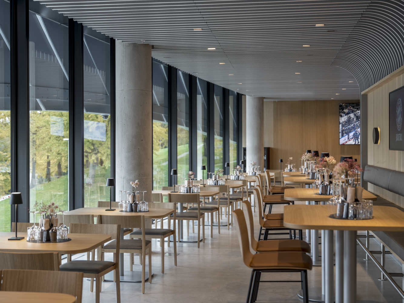 Dining hall with timber tables and chairs below a ribbed curved ceiling overlooking a green lawn