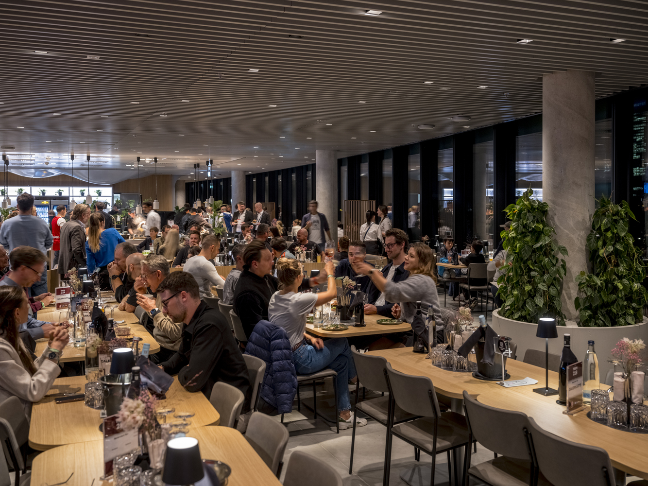 Dining hall filled with seated guests at timber tables beneath a ribbed dark ceiling