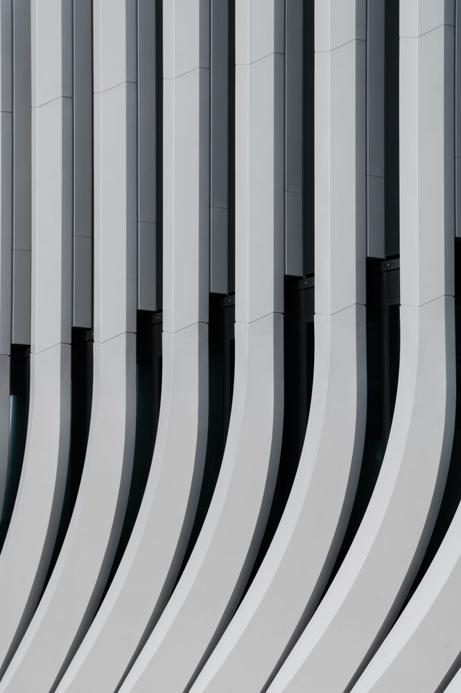 Vertical grey metal cladding fins with curved lower edges and dark recessed glazing