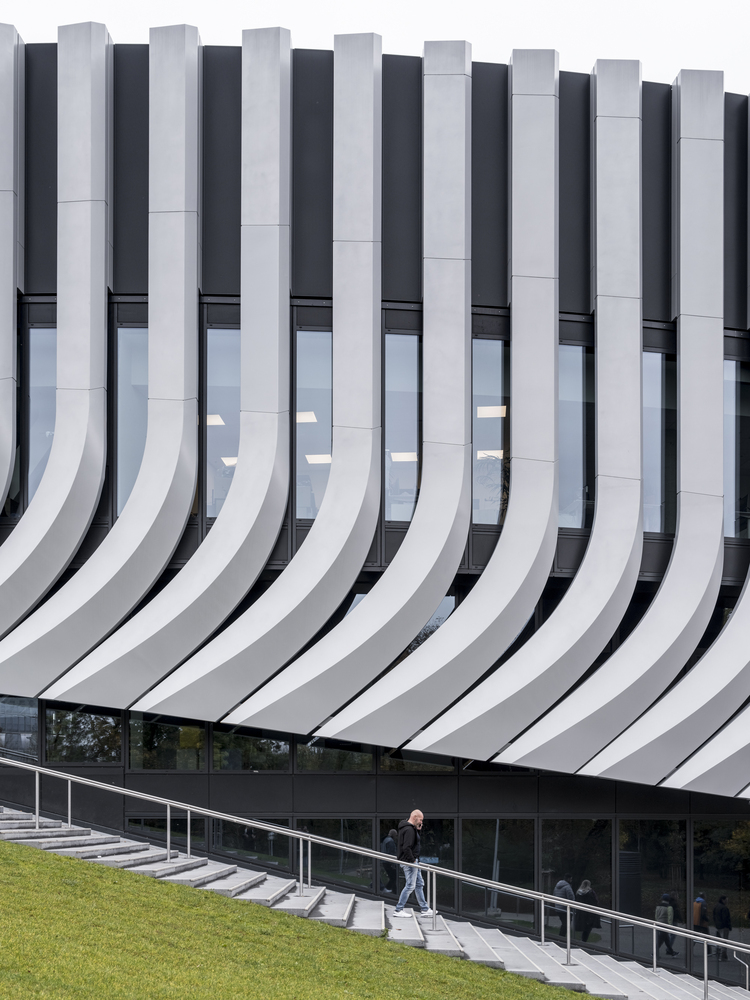 Curved facade with vertical grey and white fins above a figure on entry steps