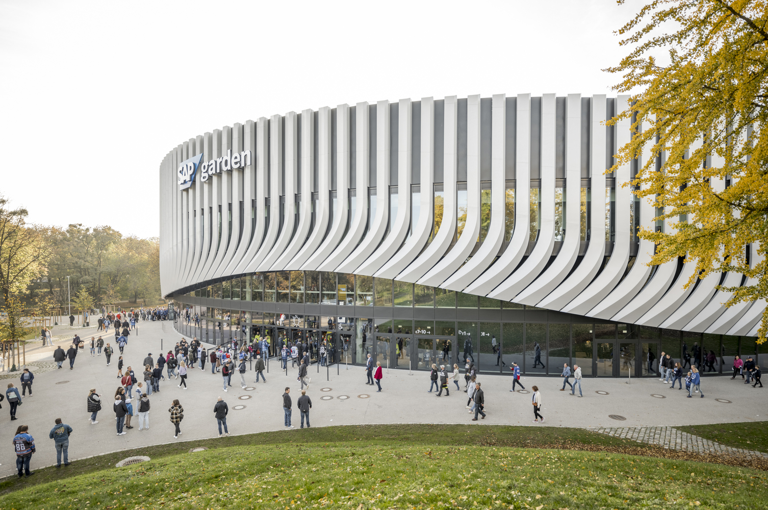 Elevated curved volume with white vertical fins above a glazed ground floor plaza with visitors