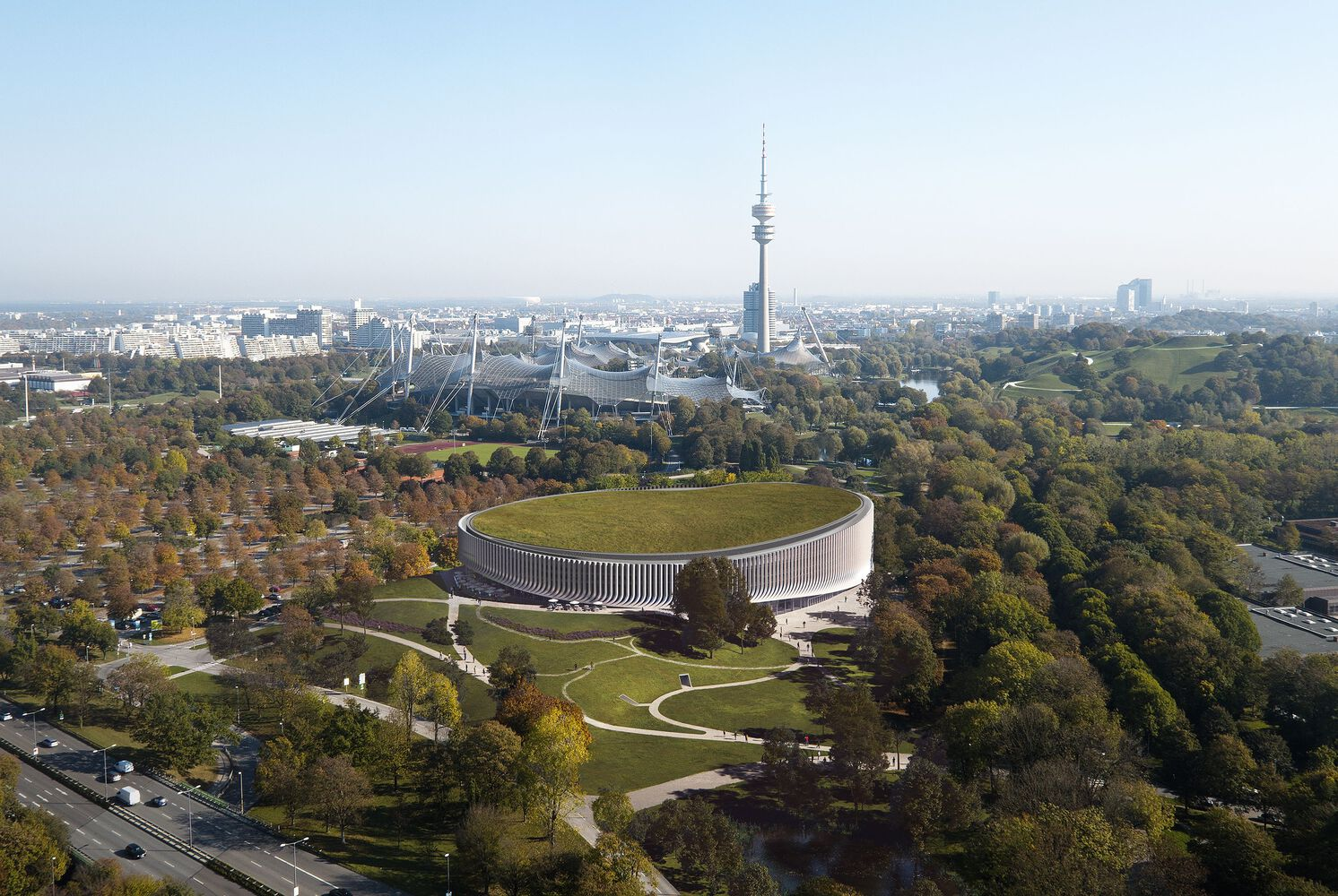 Aerial view of the elliptical green-roofed building surrounded by parkland in autumn foliage