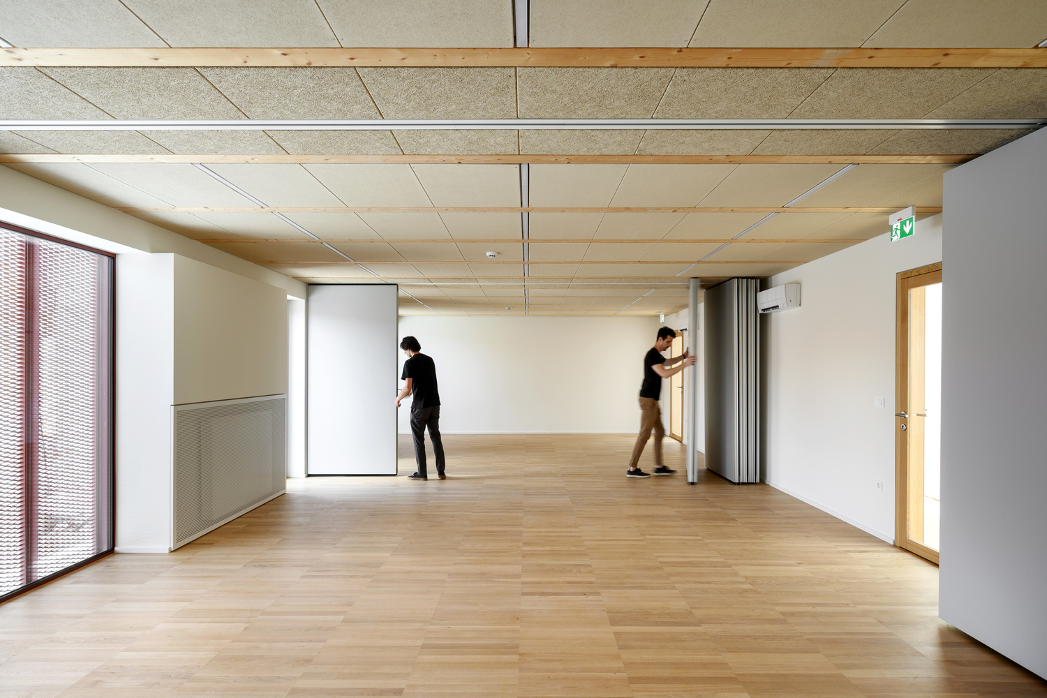Interior room with timber ceiling panels and blonde wood flooring as two people adjust partitions