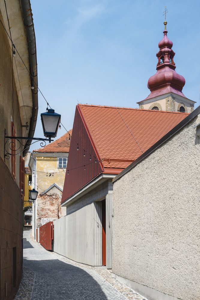 Narrow street view with white-painted timber facade beside stucco walls and church tower with orange tiles