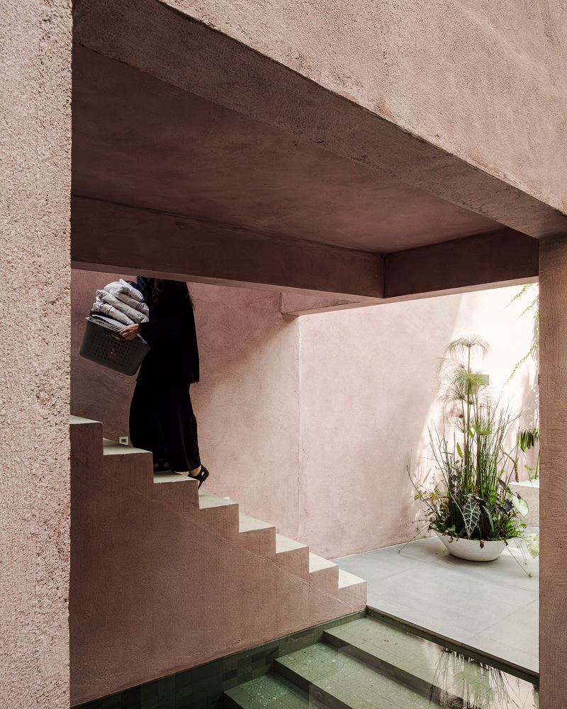 Person ascending the exterior staircase beneath the angled concrete soffit and pink stucco walls
