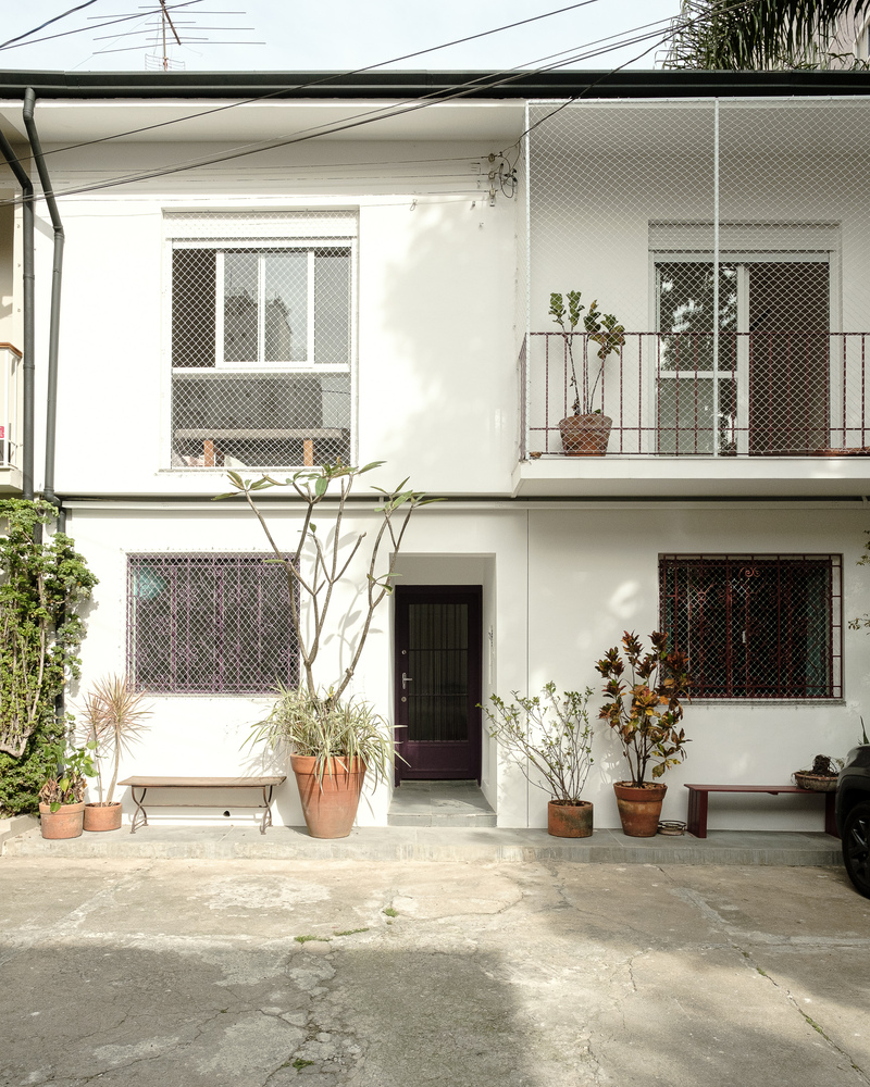 White facade with mesh-screened windows and balcony with terracotta planters in the courtyard below