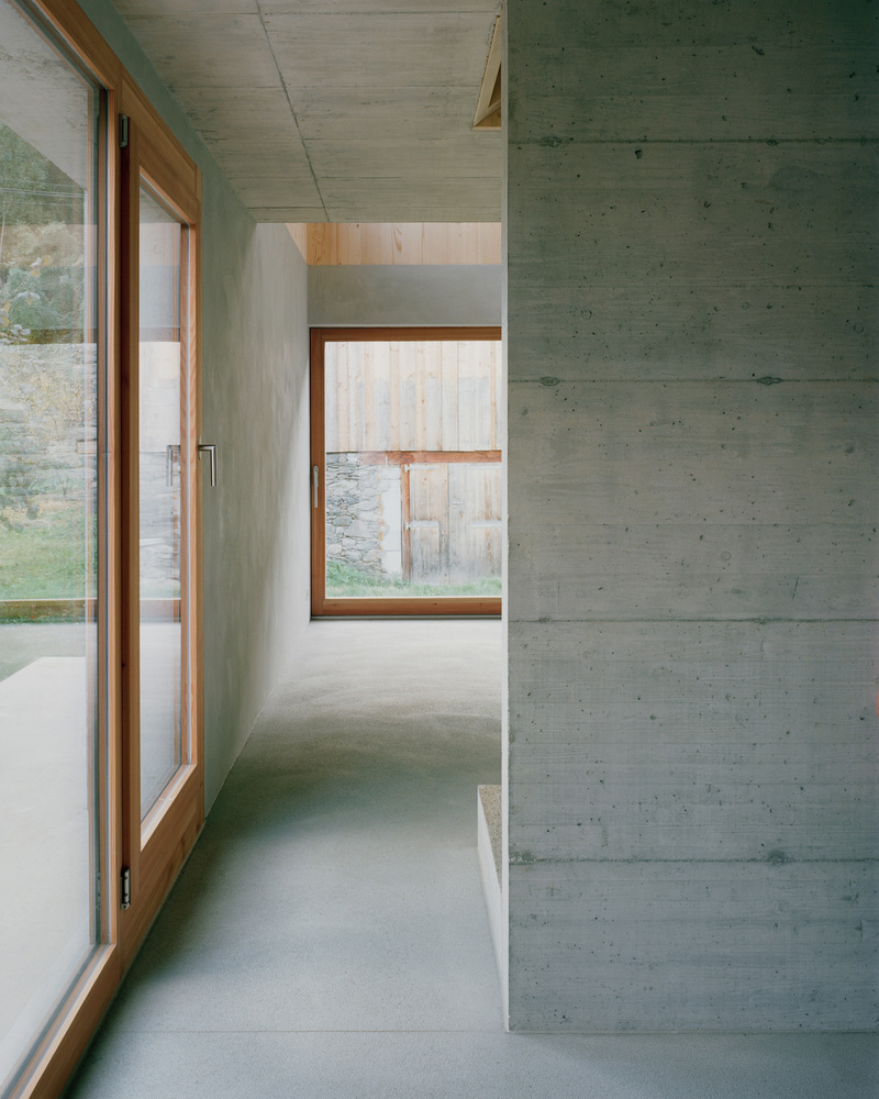 Interior corridor with board-formed concrete walls and timber-framed windows overlooking a grassy slope
