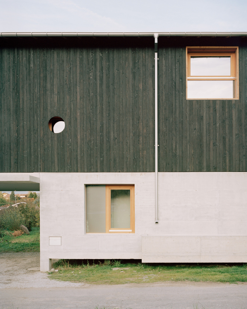 Facade with green vertical timber cladding over white concrete base and circular window detail