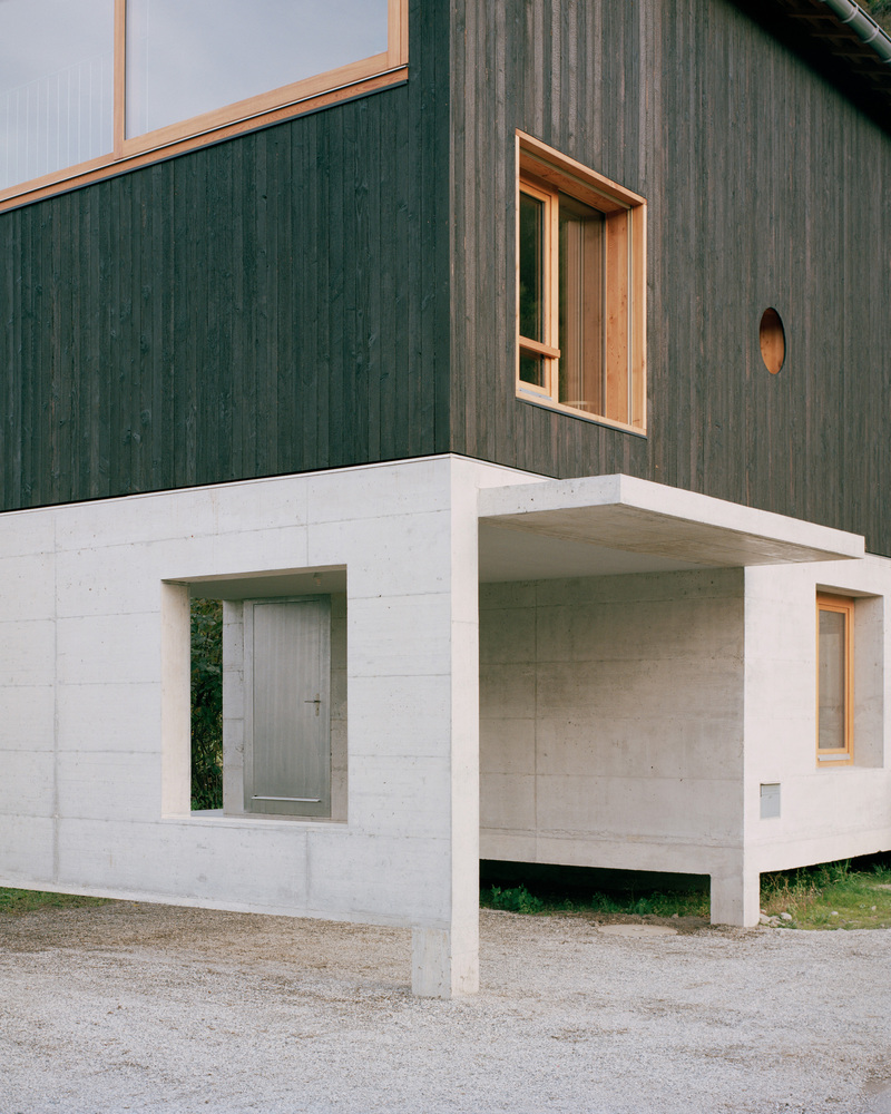Corner view showing timber-clad upper floor on concrete pilotis with recessed entrance below