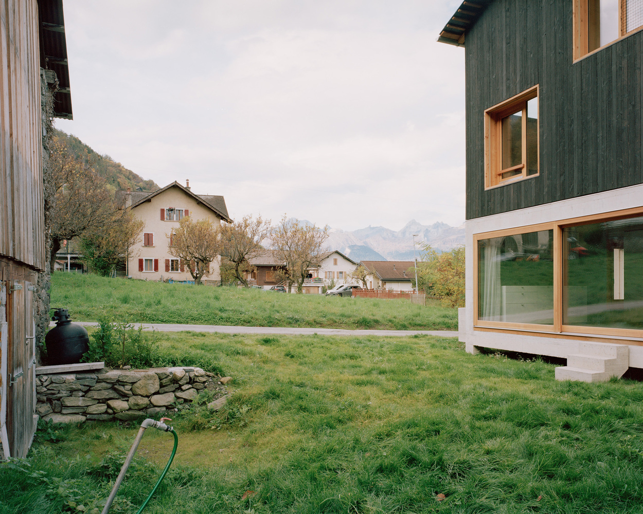View across a grassy hillside showing the concrete base and green timber upper volume