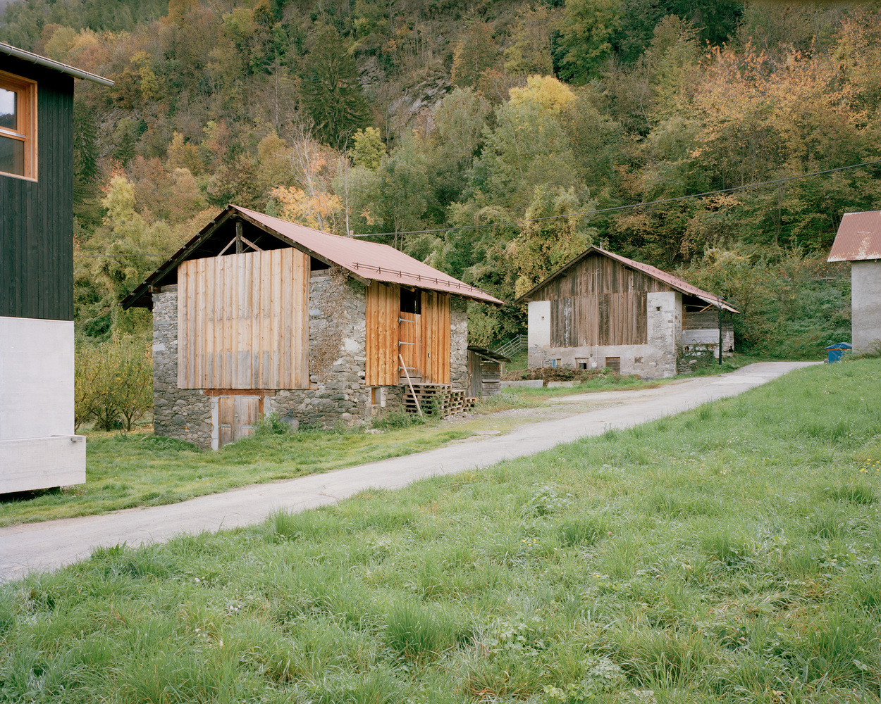 Rural lane with traditional stone and timber barns against an autumn forest hillside