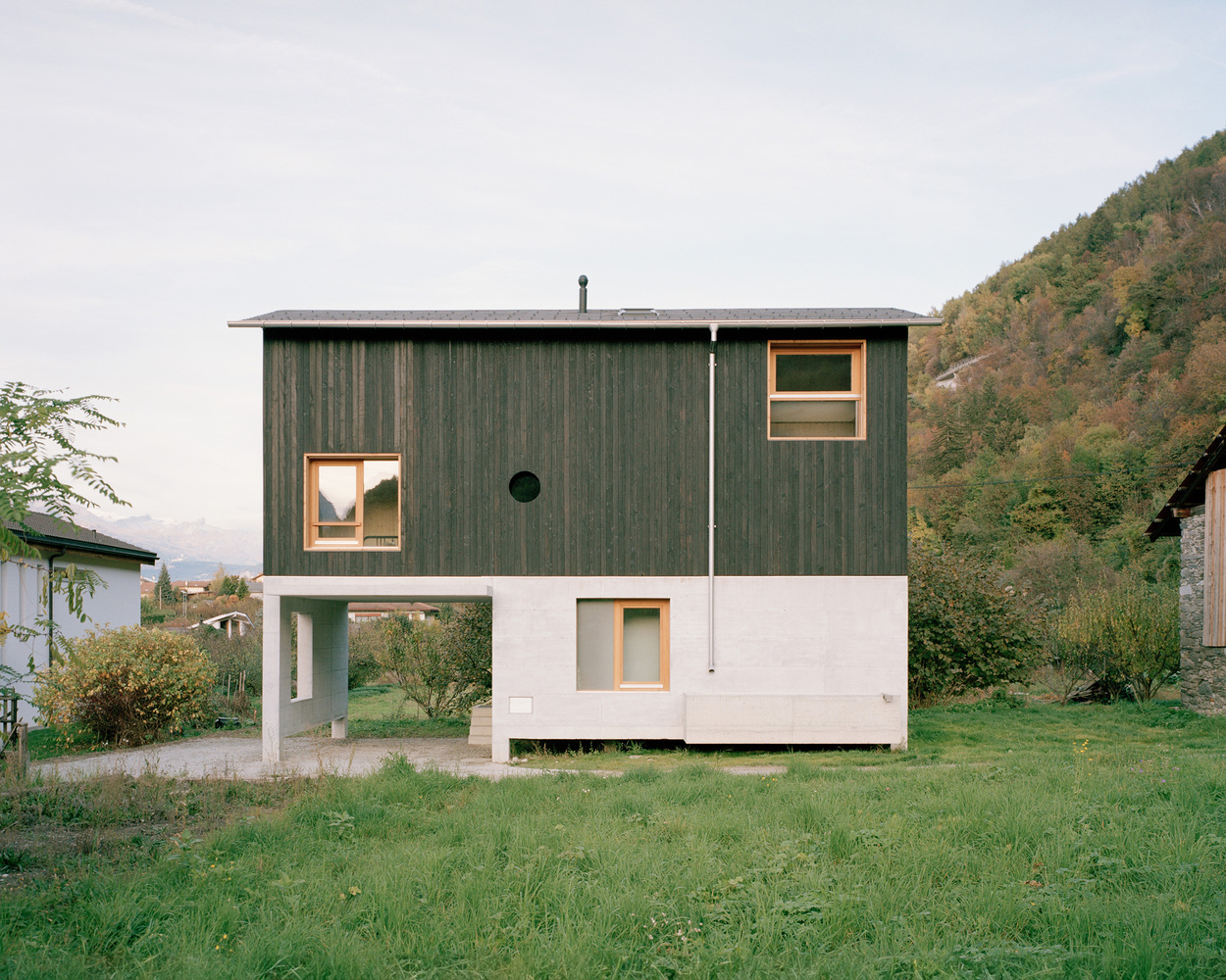 Two-storey elevation with dark timber cladding above a white plaster base set in a hillside lawn