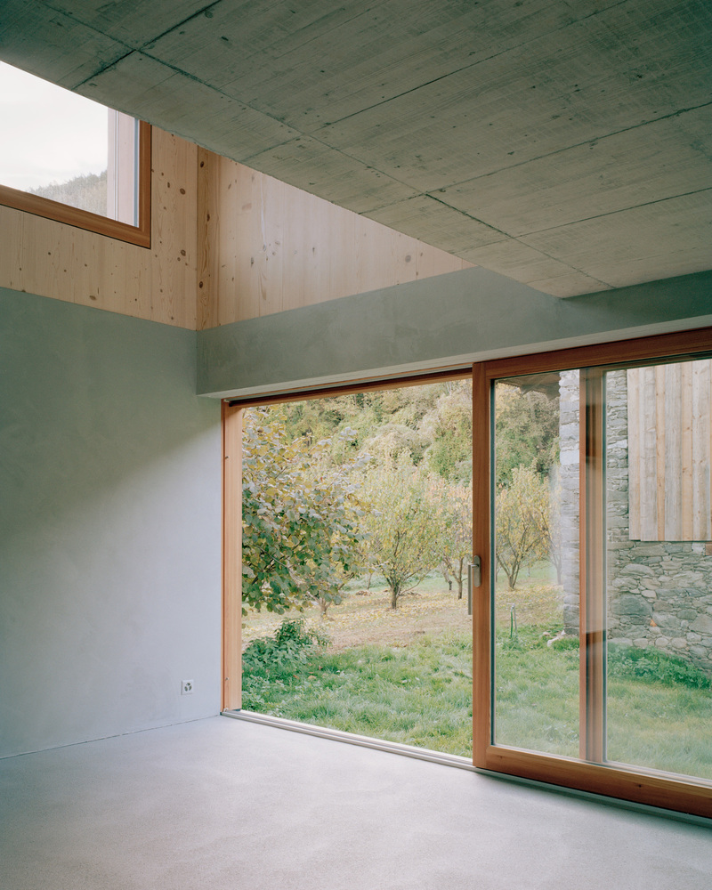 Interior corner with timber-framed sliding doors overlooking an orchard through concrete walls