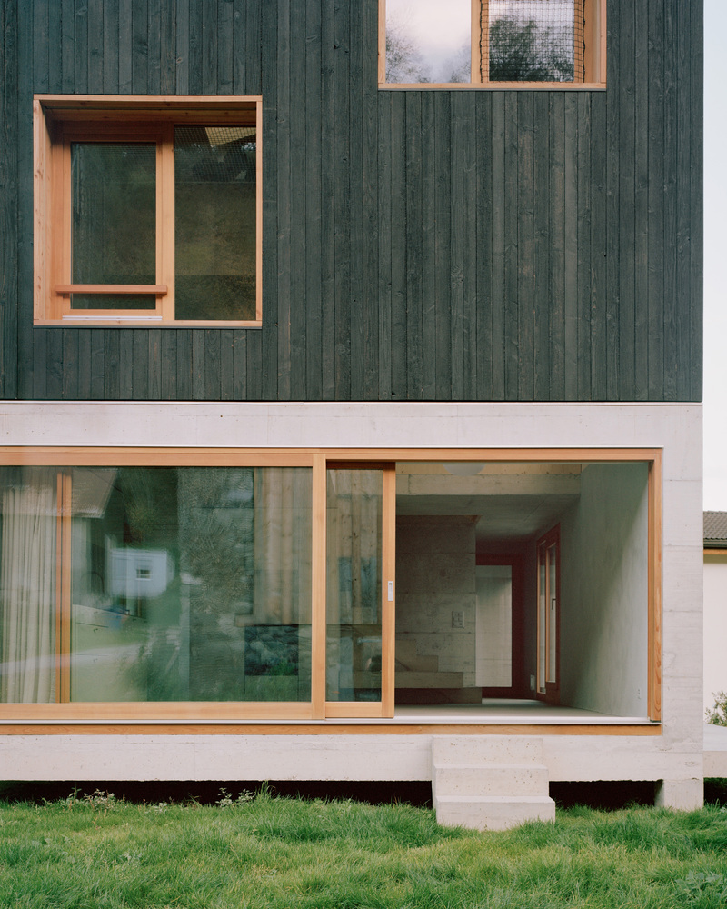 Facade detail showing timber window frames set in dark vertical cladding and white concrete base