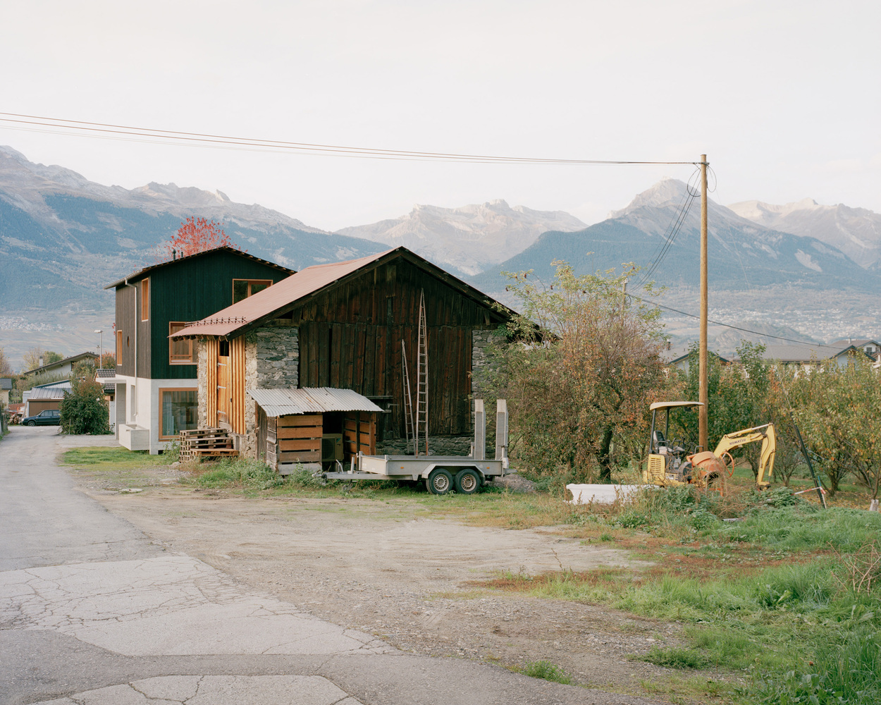 Existing barn structure with corrugated metal siding and a trailer parked alongside in an alpine valley