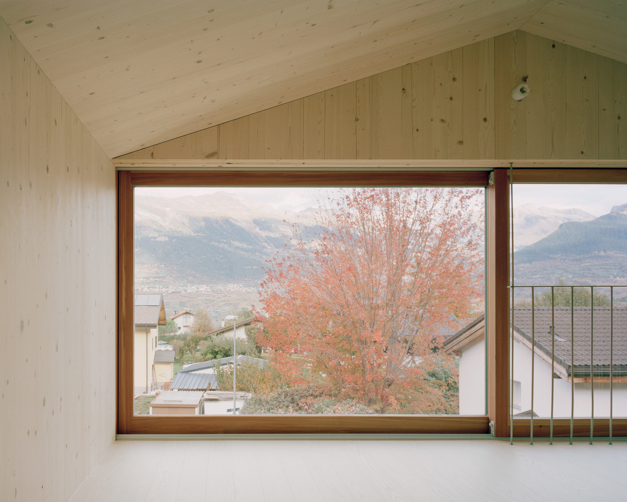 Horizontal window framing distant mountains and an orange-leaved tree in the foreground during autumn