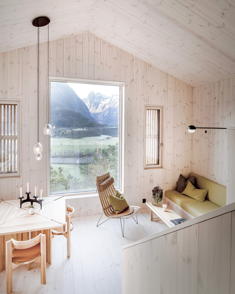 Living room with vertical wood paneling and tall window framing a glacial lake and snowy peaks