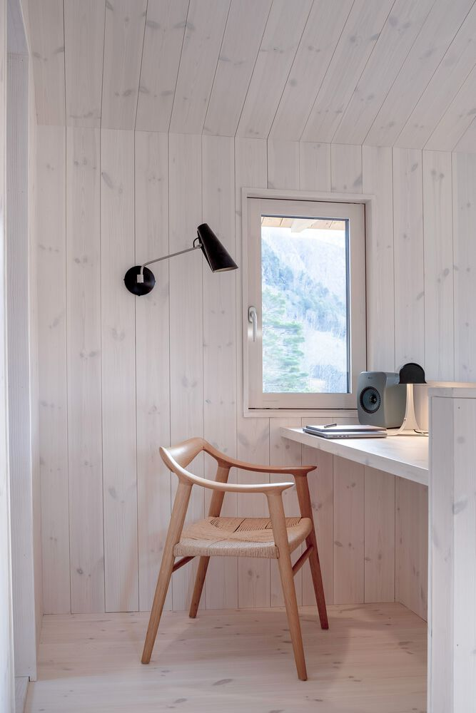 Small desk nook with built-in ledge and pivoting wall lamp beside a window overlooking water