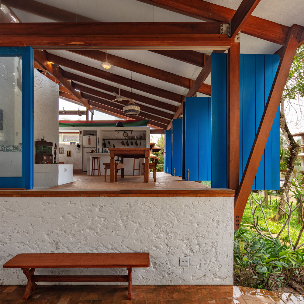 View from half-height white wall showing exposed timber frame, blue painted columns, and continuous interior to exterior terracotta flooring
