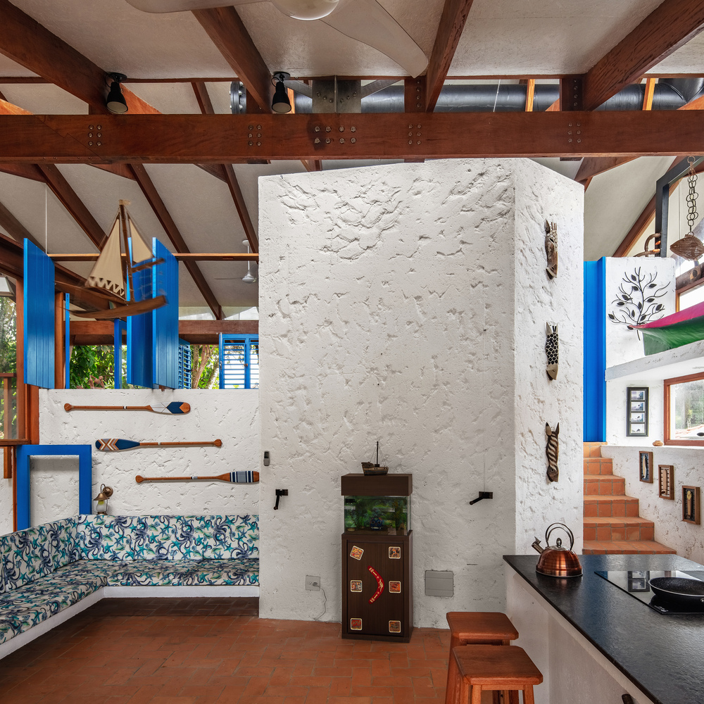 Interior showing thick white masonry chimney core, timber stair, built-in sofa, and exposed beam ceiling with steel connectors