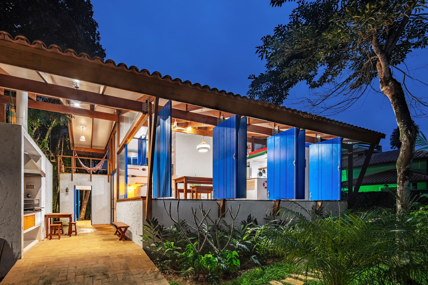 Covered exterior walkway leading to blue-shuttered facade with exposed timber rafters at twilight