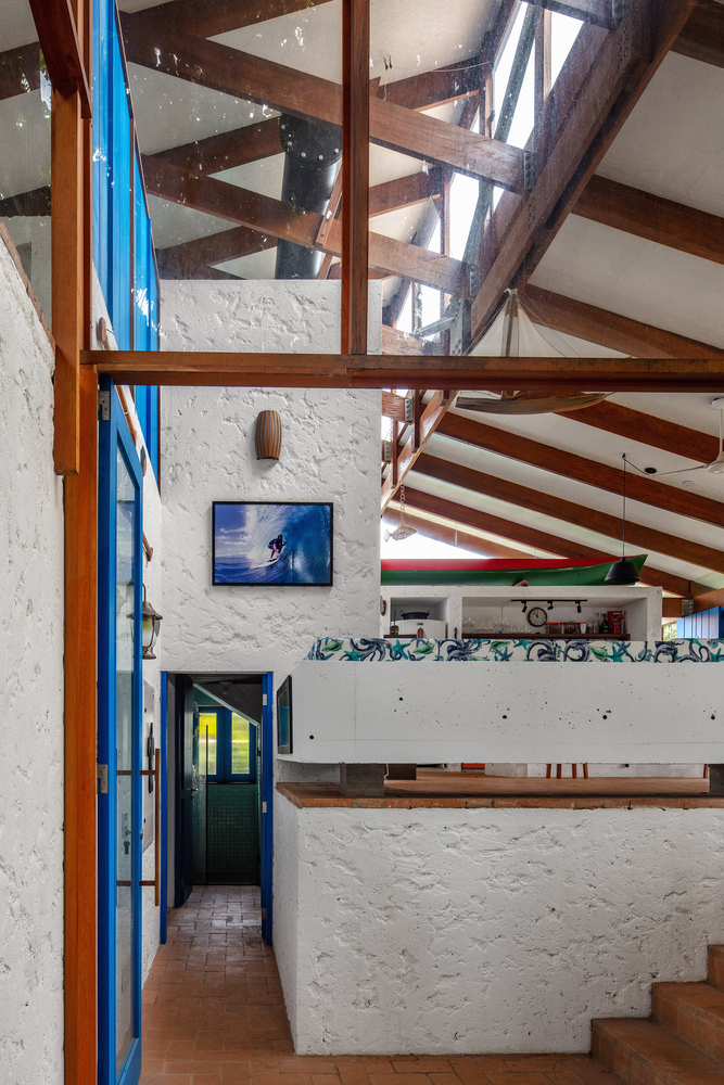 Double-height interior with exposed timber rafters, white painted masonry walls, and a sleeping loft under skylights