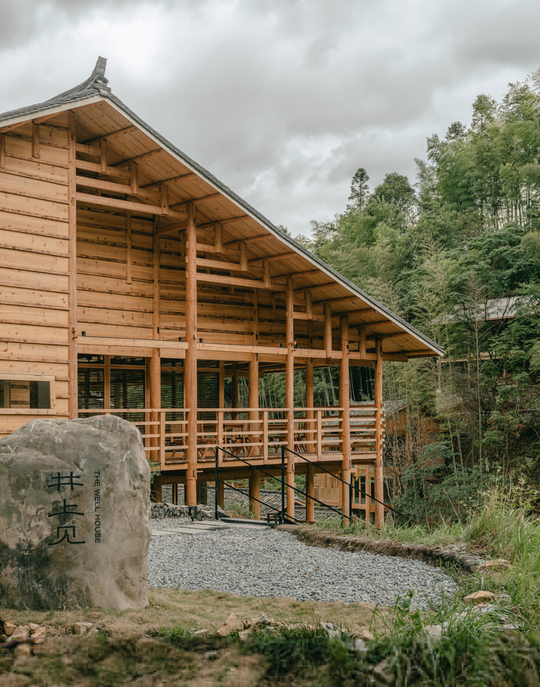 Elevated timber building with exposed structural frame and open verandah beside a carved stone marker
