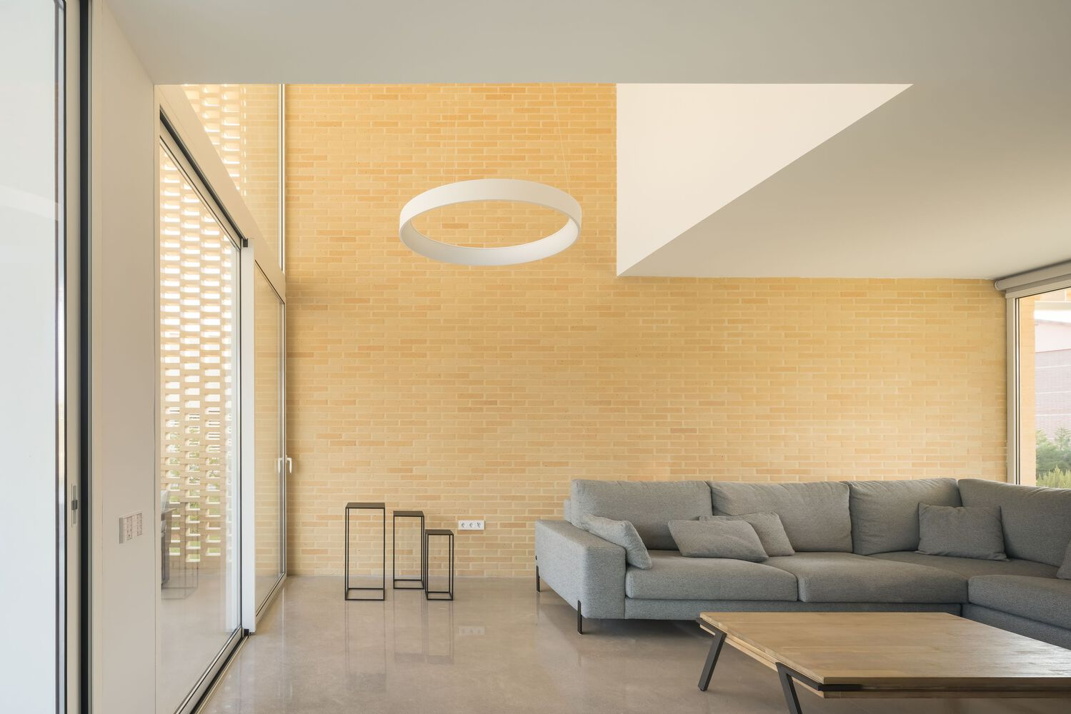 Living room with yellow brick wall, circular pendant light and grey sofa at dusk