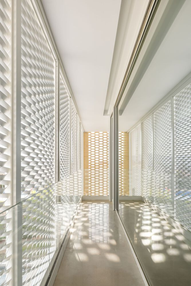 Narrow corridor with perforated white screens casting dappled sunlight on the polished floor