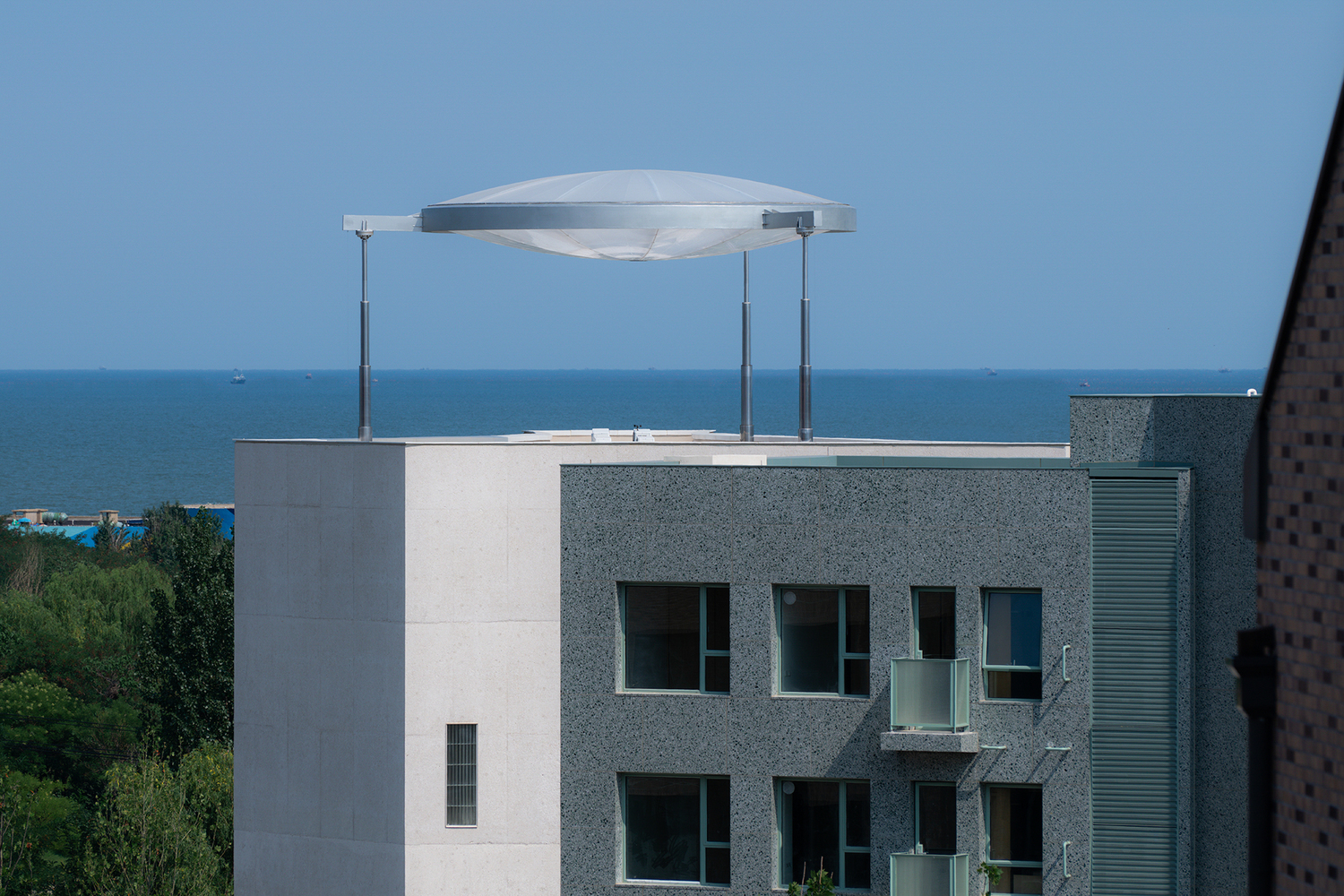 Rooftop terrace with curved metal canopy on slender posts overlooking the sea