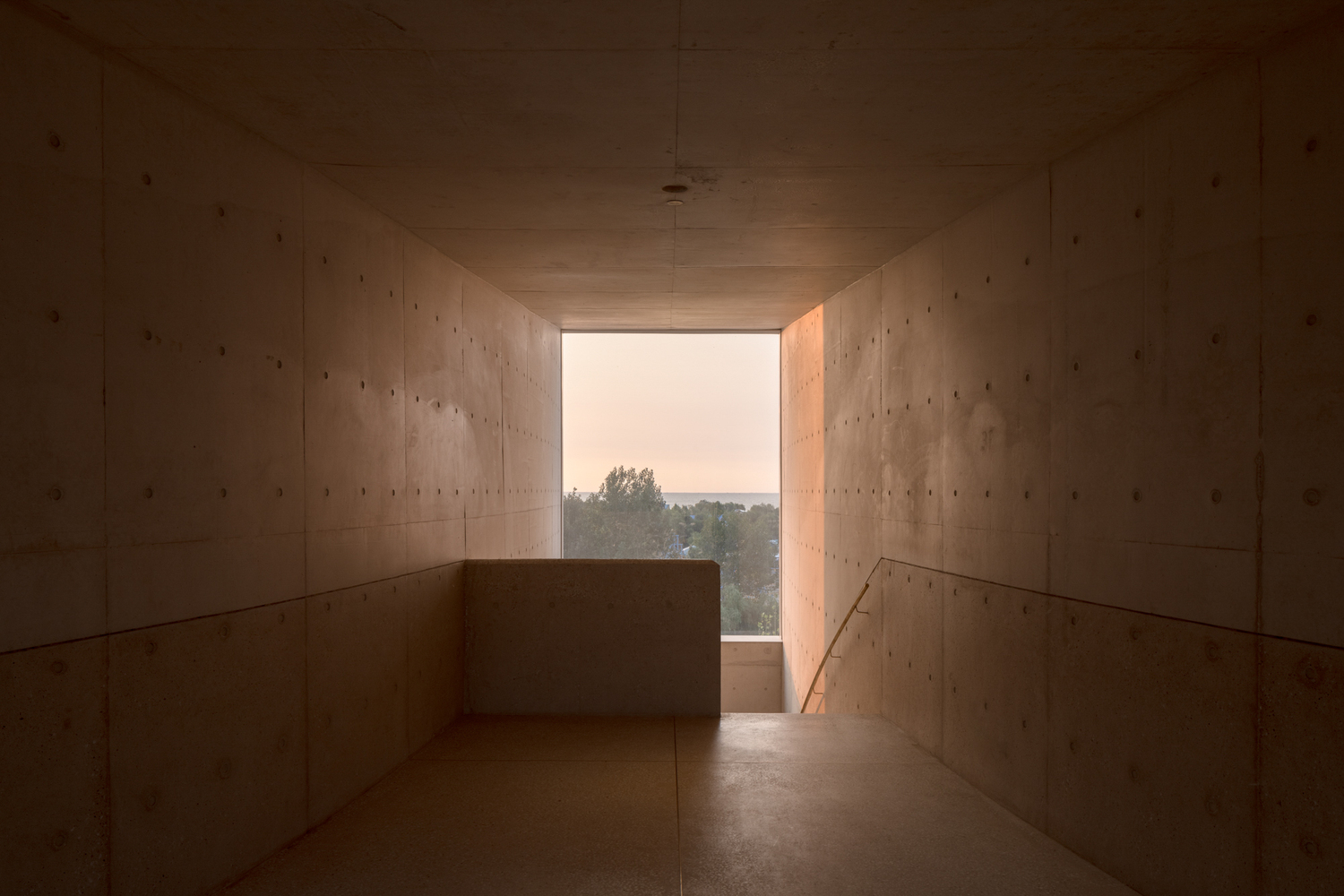 Concrete corridor framing distant landscape view through opening at dusk
