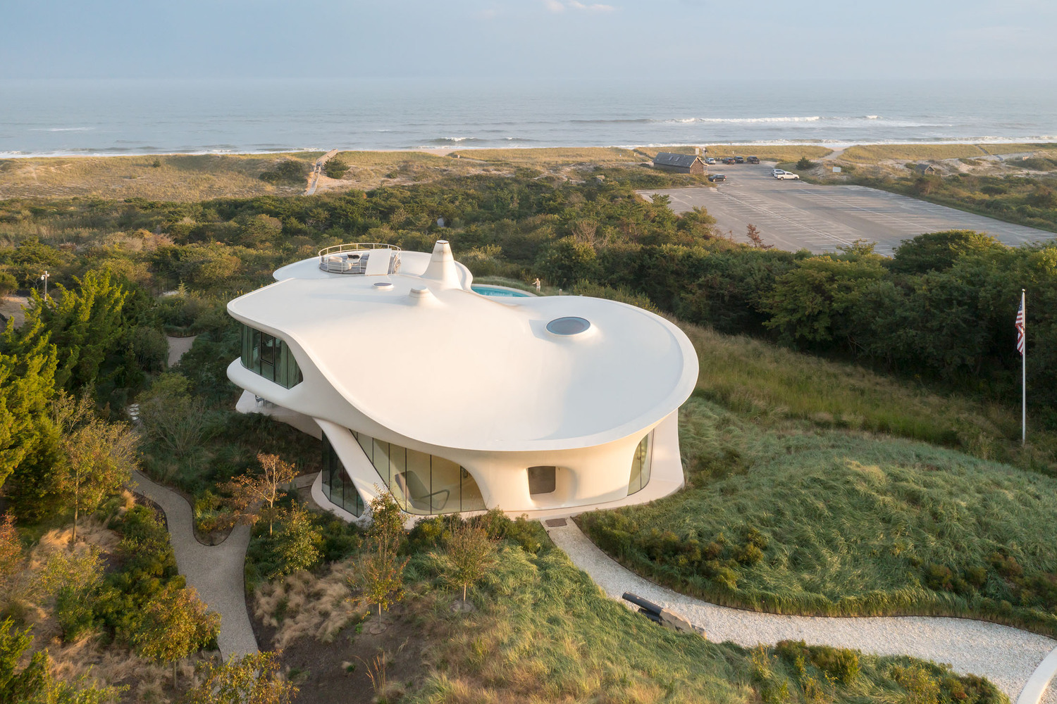 Aerial view of the white curved roof with circular skylights nestled among coastal dunes and vegetation