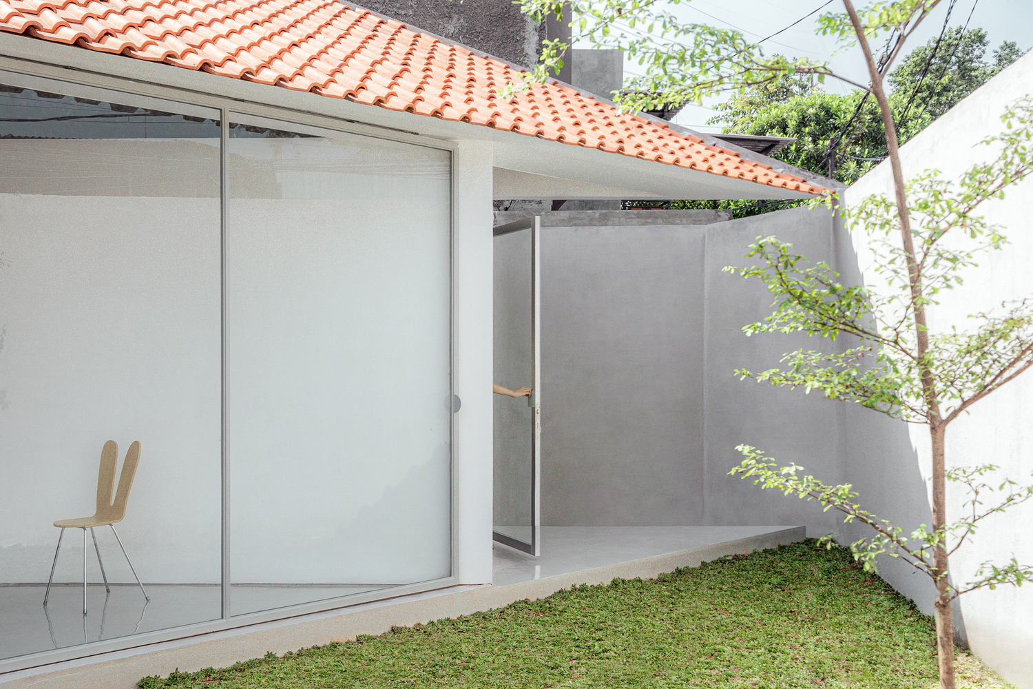 Courtyard view with sliding glass doors, terra-cotta tiled roof and a young tree in the lawn